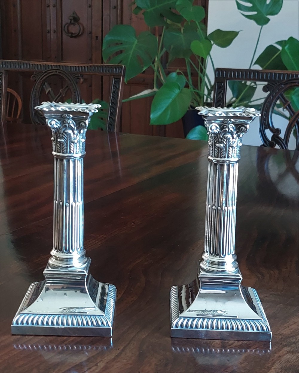 A pair of sterling silver candlesticks designed in the form of Corinthian columns with fluted shafts and stepped square bases holding white taper candles. View II
