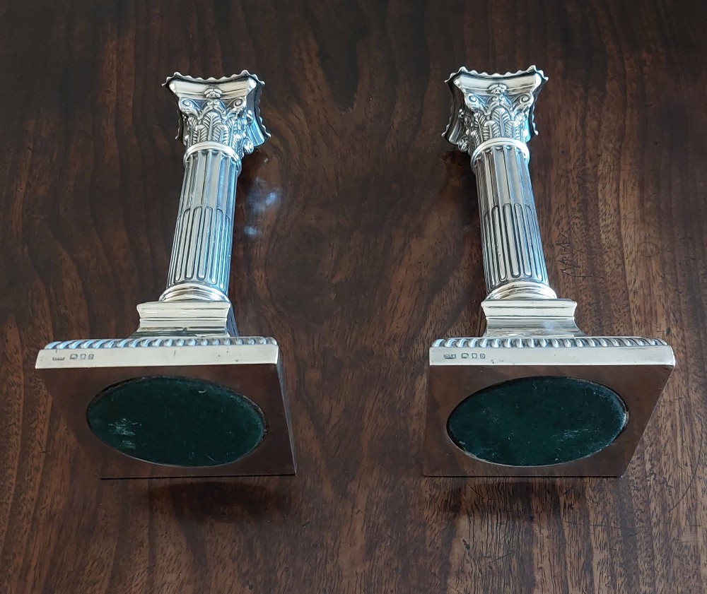 A pair of sterling silver candlesticks designed in the form of Corinthian columns with fluted shafts and stepped square bases holding white taper candles. View III