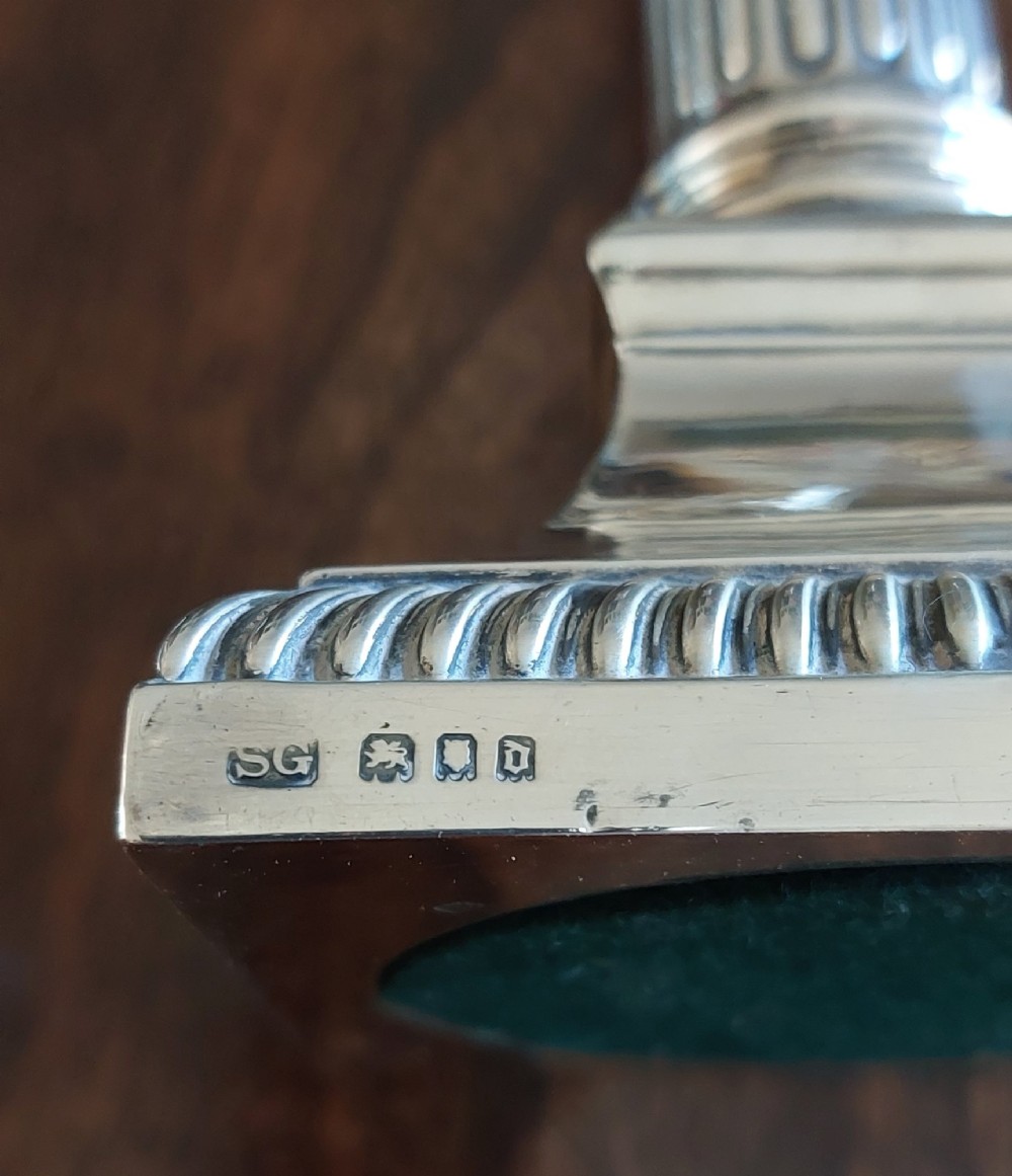 A pair of sterling silver candlesticks designed in the form of Corinthian columns with fluted shafts and stepped square bases holding white taper candles. View IV