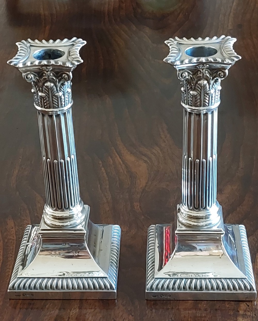 A pair of sterling silver candlesticks designed in the form of Corinthian columns with fluted shafts and stepped square bases holding white taper candles. View VII