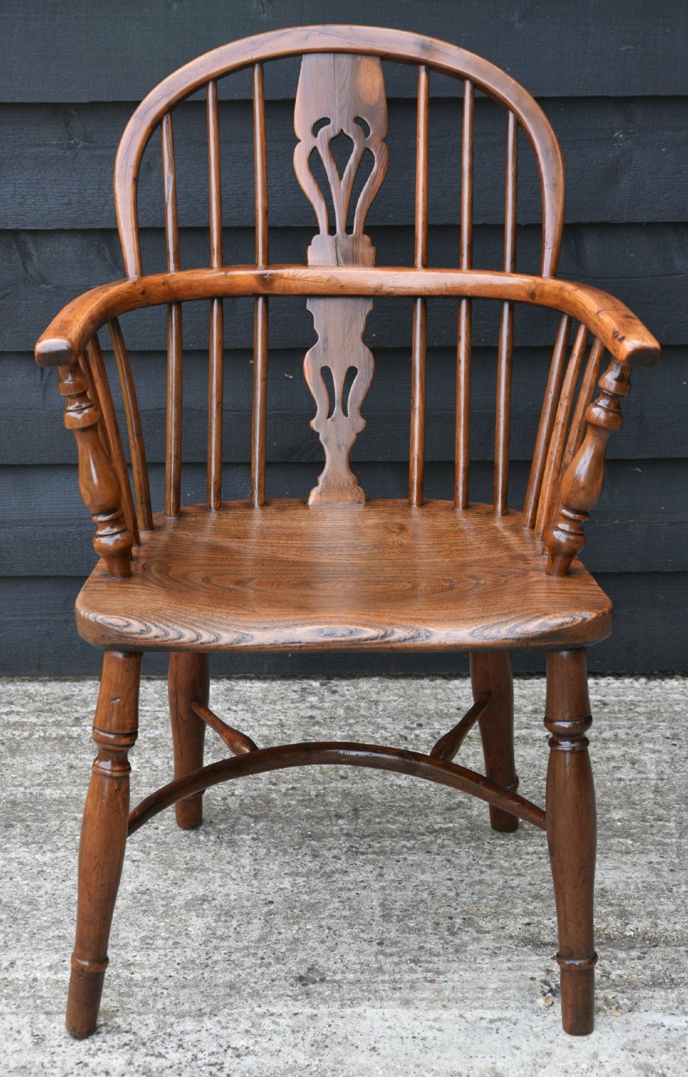 A 19th-century English Windsor armchair made from yew and elm wood featuring a hoop back, a central pierced splat, turned legs, and a crinoline stretcher.