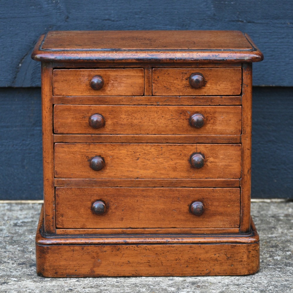 A Victorian mahogany miniature chest of drawers featuring two short over three long drawers with turned wooden knobs resting on a plinth base.