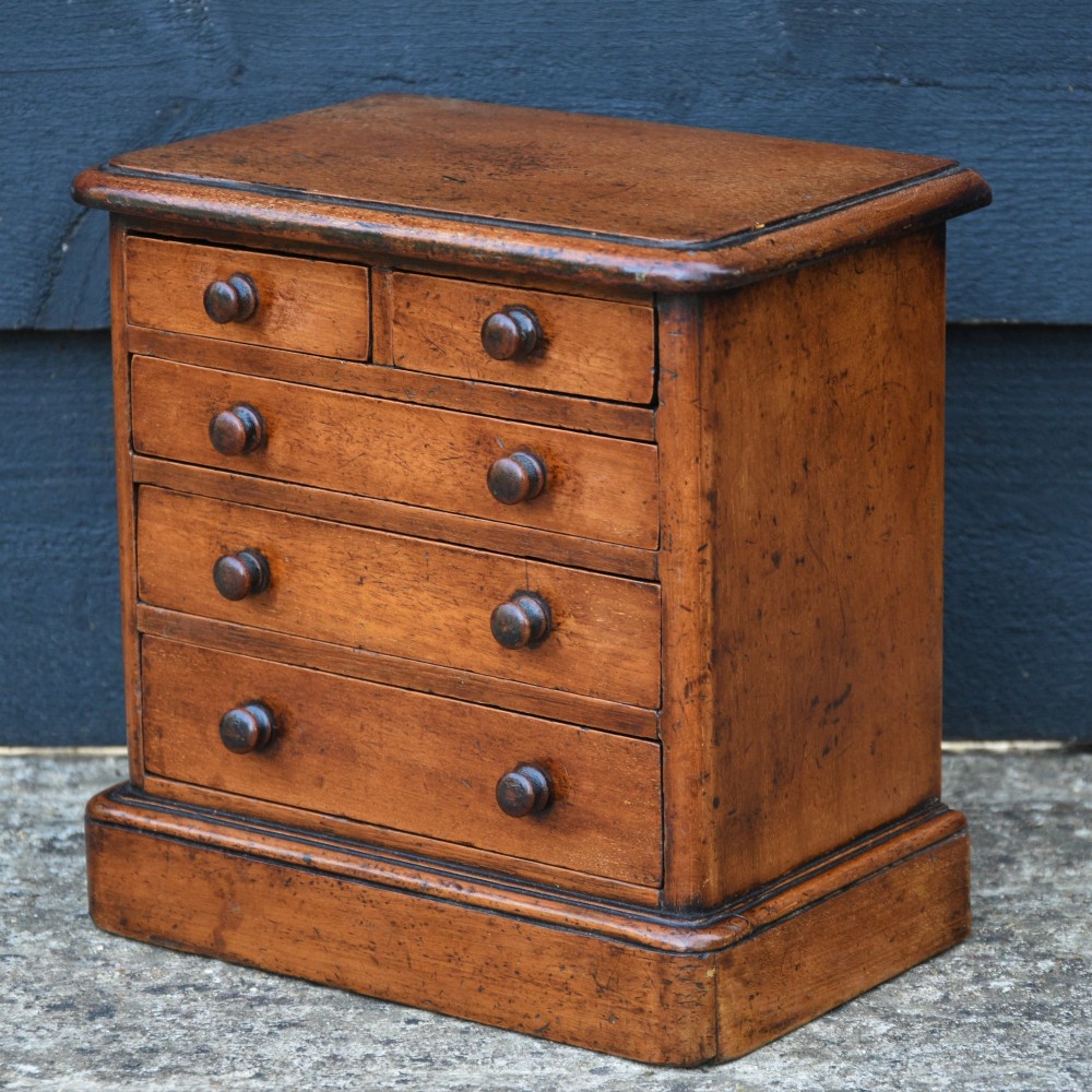 A Victorian mahogany miniature chest of drawers featuring two short over three long drawers with turned wooden knobs resting on a plinth base. View II