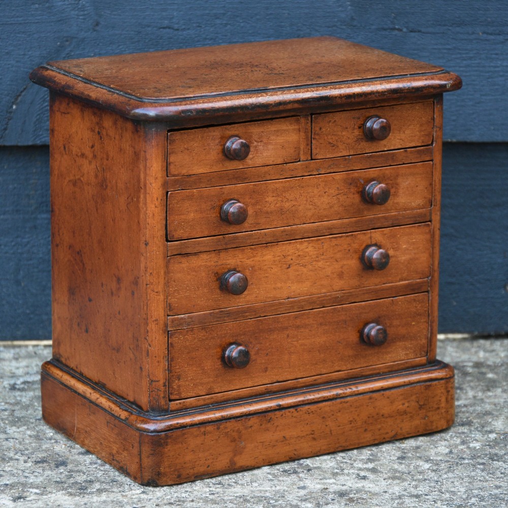 A Victorian mahogany miniature chest of drawers featuring two short over three long drawers with turned wooden knobs resting on a plinth base. View III