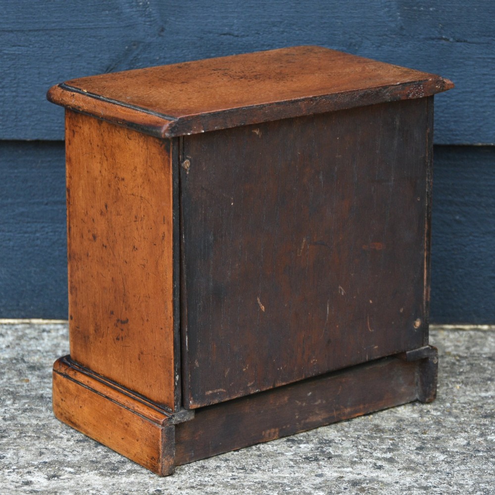 A Victorian mahogany miniature chest of drawers featuring two short over three long drawers with turned wooden knobs resting on a plinth base. View IV