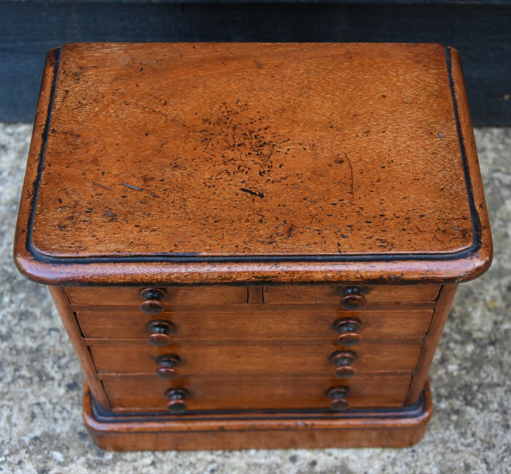 A Victorian mahogany miniature chest of drawers featuring two short over three long drawers with turned wooden knobs resting on a plinth base. View V