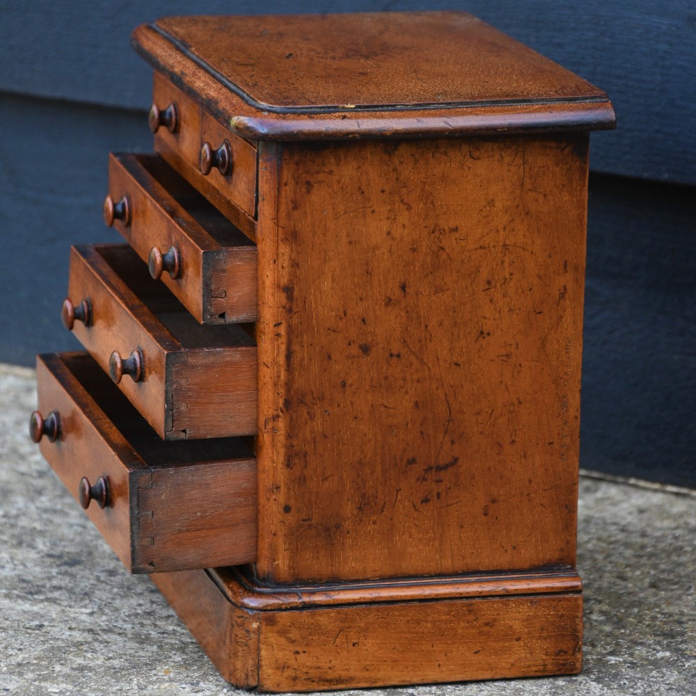 A Victorian mahogany miniature chest of drawers featuring two short over three long drawers with turned wooden knobs resting on a plinth base. View VI