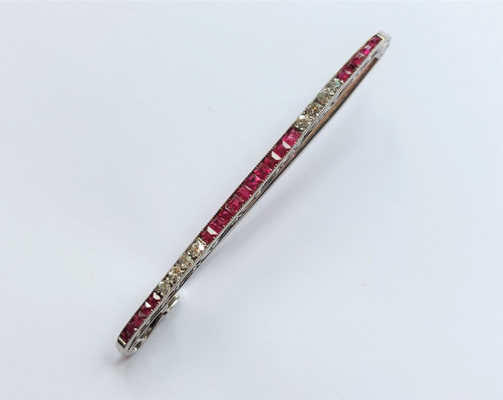 An Art Deco slender bar brooch crafted in white metal, channel-set with square red rubies interspersed with small round diamonds with millegrain detailing.