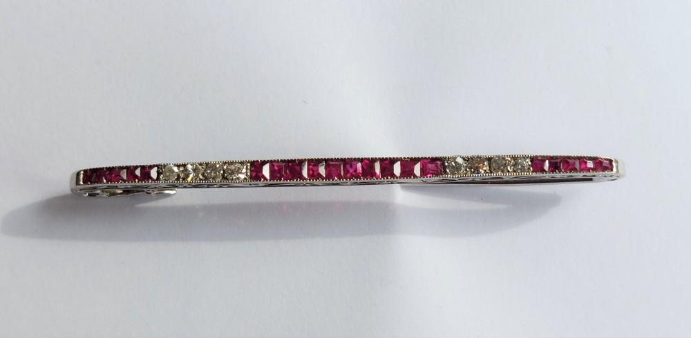 An Art Deco slender bar brooch crafted in white metal, channel-set with square red rubies interspersed with small round diamonds with millegrain detailing. View II