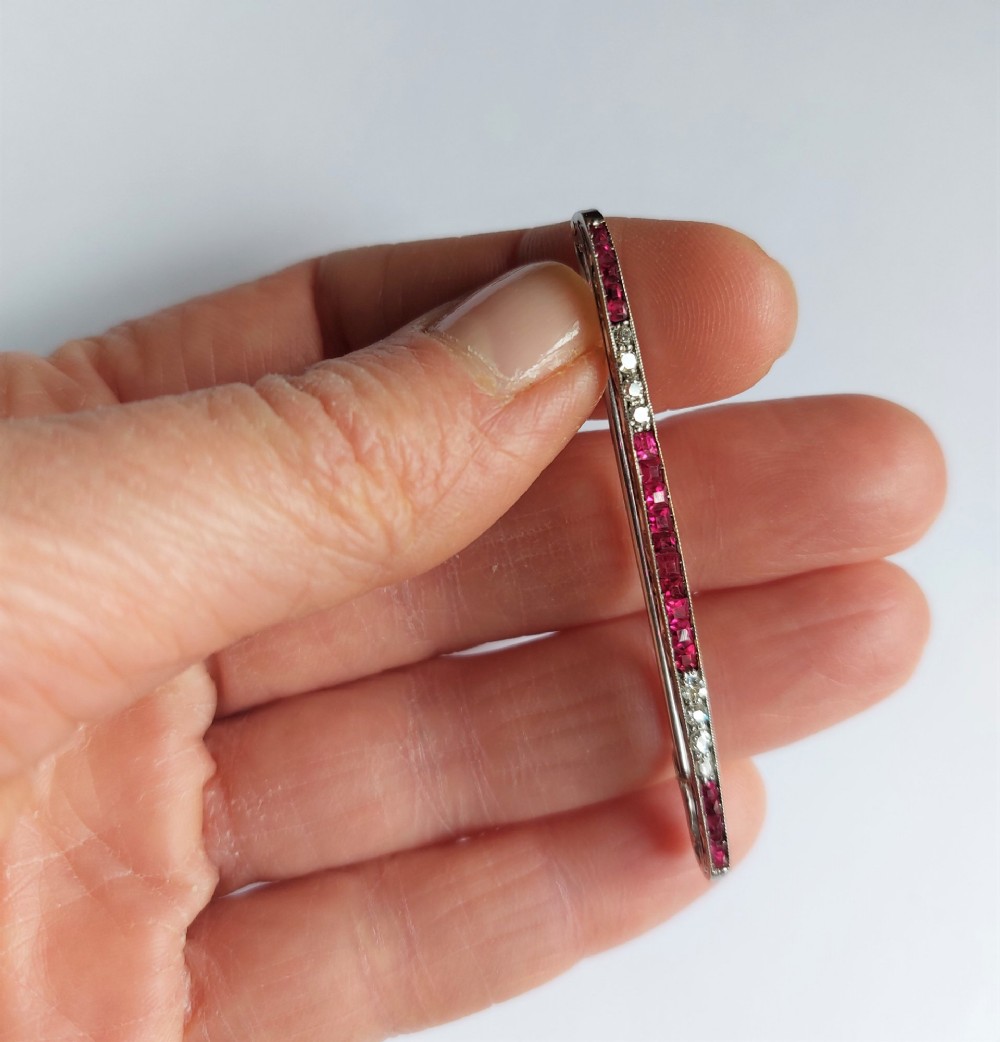 An Art Deco slender bar brooch crafted in white metal, channel-set with square red rubies interspersed with small round diamonds with millegrain detailing. View III