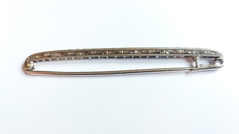 An Art Deco slender bar brooch crafted in white metal, channel-set with square red rubies interspersed with small round diamonds with millegrain detailing. View IV
