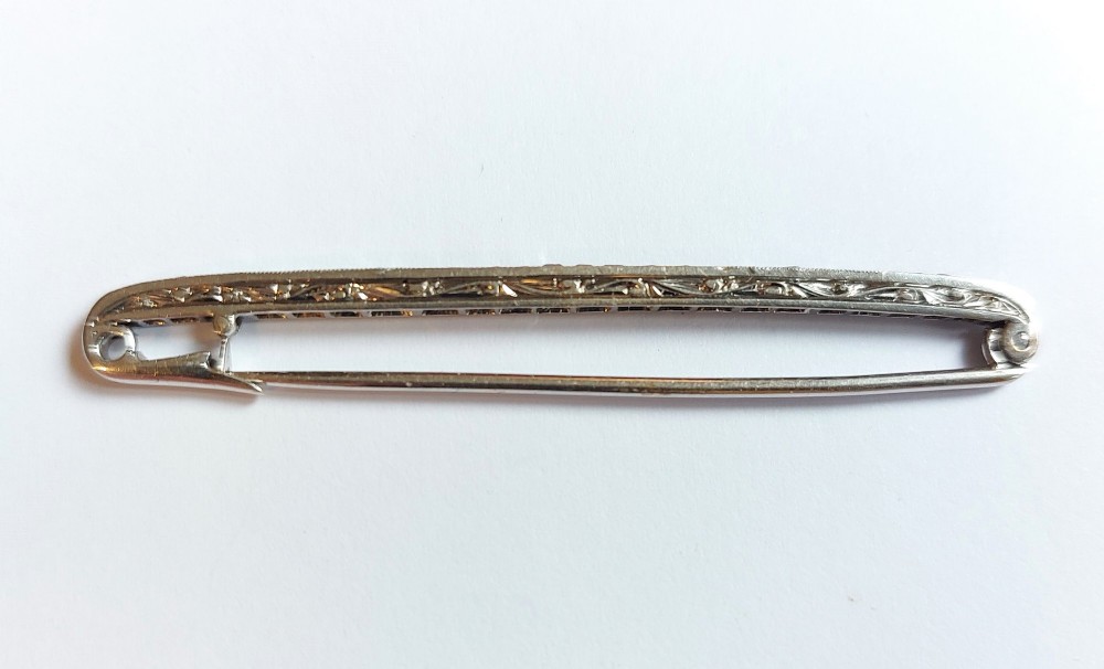 An Art Deco slender bar brooch crafted in white metal, channel-set with square red rubies interspersed with small round diamonds with millegrain detailing. View V