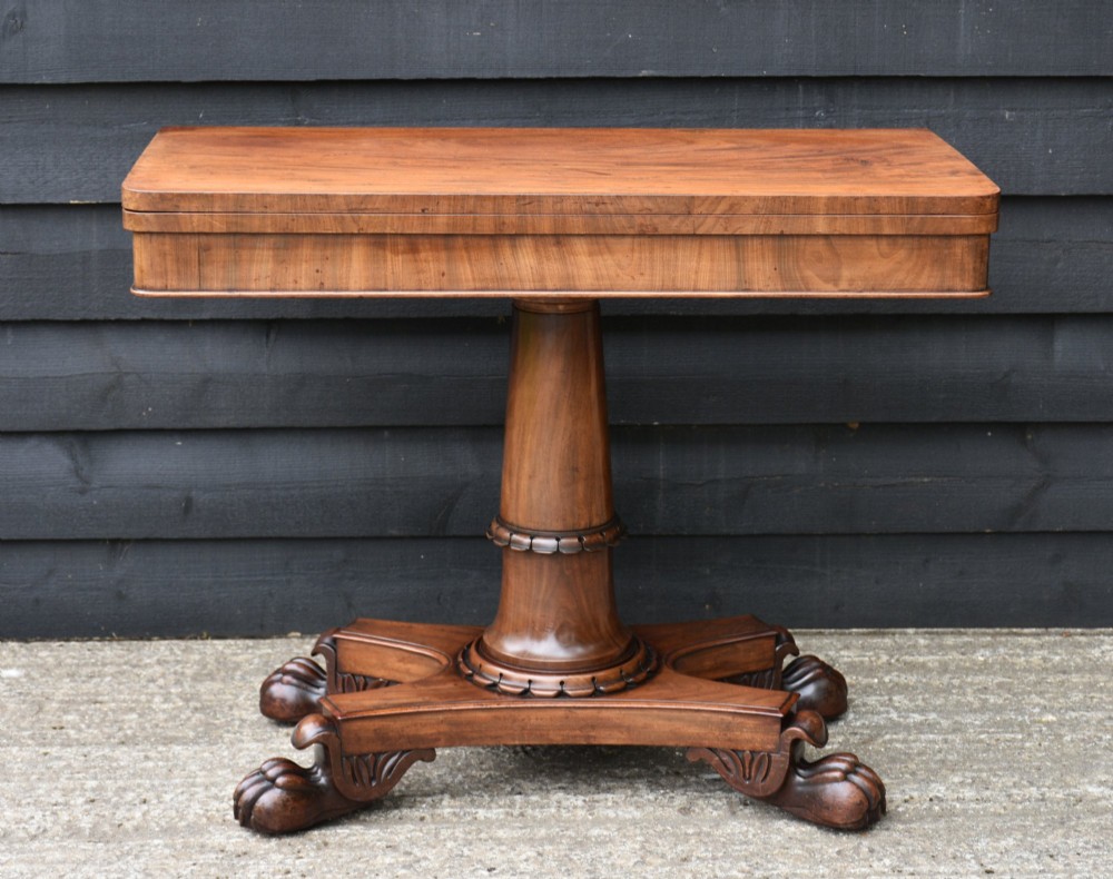 A 19th-century William IV mahogany fold-over card table featuring a rectangular swivel top resting on a tapered pedestal column and quadform base with carved lion paw feet.