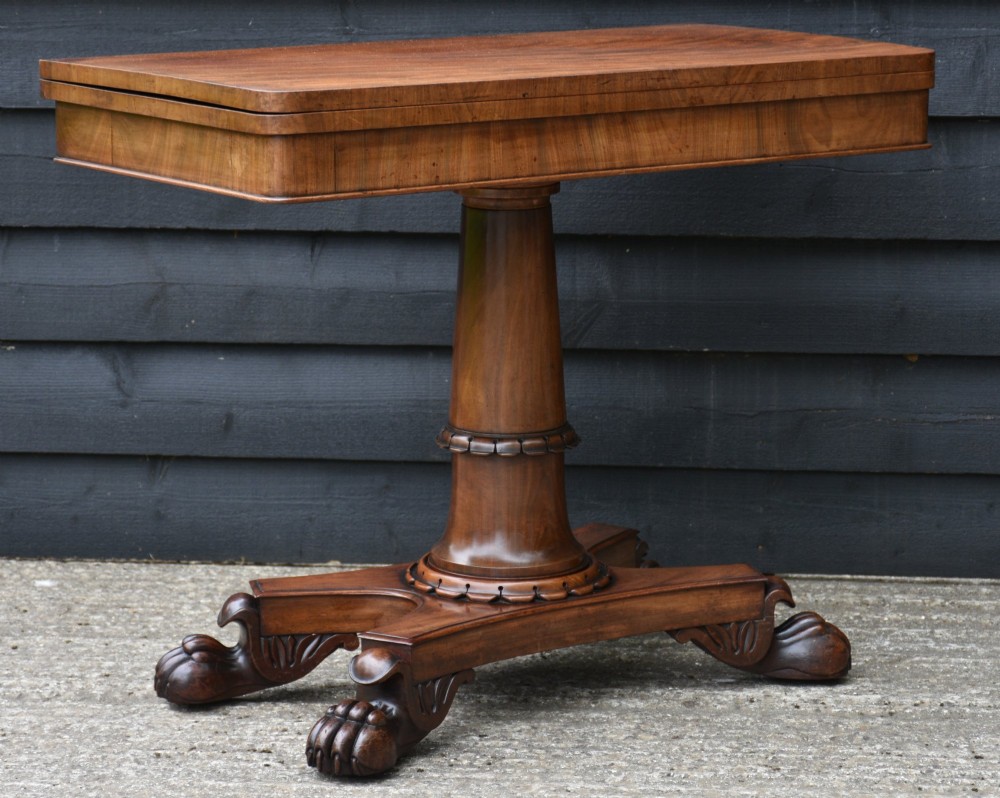 A 19th-century William IV mahogany fold-over card table featuring a rectangular swivel top resting on a tapered pedestal column and quadform base with carved lion paw feet. View V