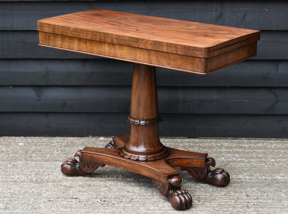 A 19th-century William IV mahogany fold-over card table featuring a rectangular swivel top resting on a tapered pedestal column and quadform base with carved lion paw feet. View VI