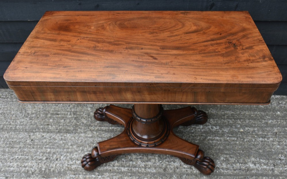 A 19th-century William IV mahogany fold-over card table featuring a rectangular swivel top resting on a tapered pedestal column and quadform base with carved lion paw feet. View X