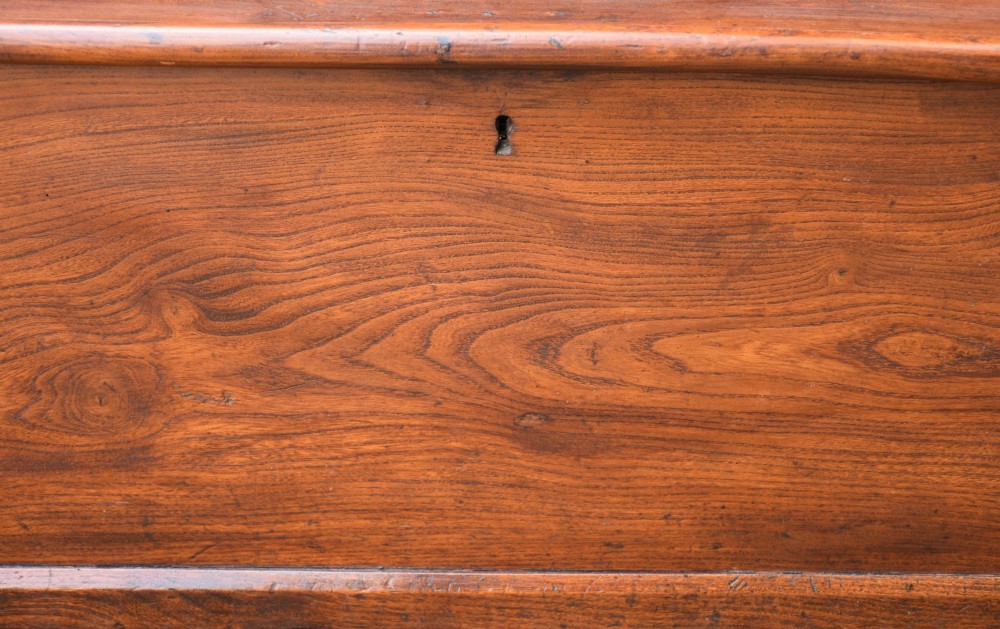 A rectangular Georgian elm blanket box featuring a hinged top lid, front keyhole, side iron handles, and a simple plinth base. View III