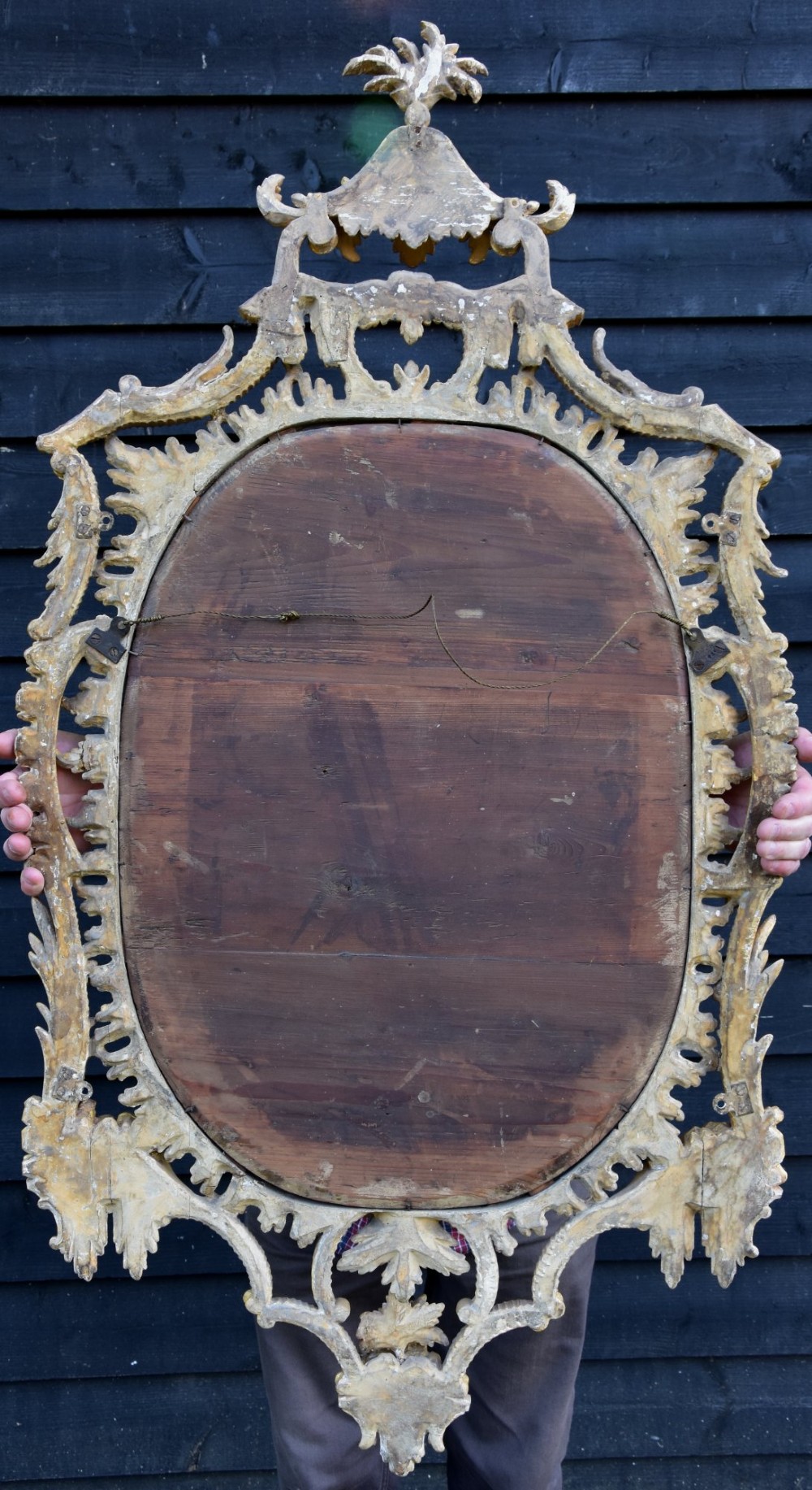 An 18th-century Georgian giltwood wall mirror featuring an oval mirror plate surrounded by an intricately carved gold leaf frame with acanthus leaf cresting and C-scroll motifs. View II