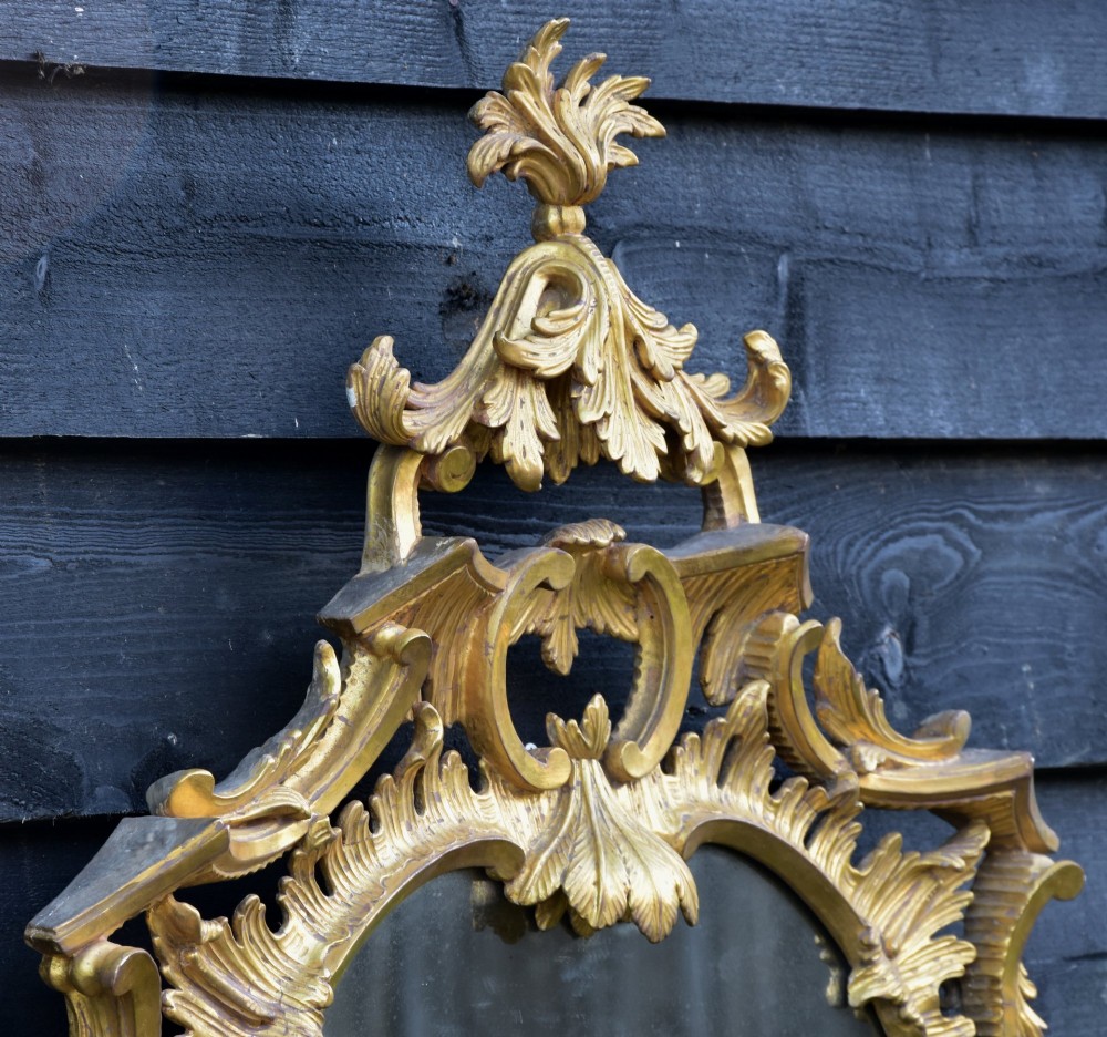 An 18th-century Georgian giltwood wall mirror featuring an oval mirror plate surrounded by an intricately carved gold leaf frame with acanthus leaf cresting and C-scroll motifs. View IV