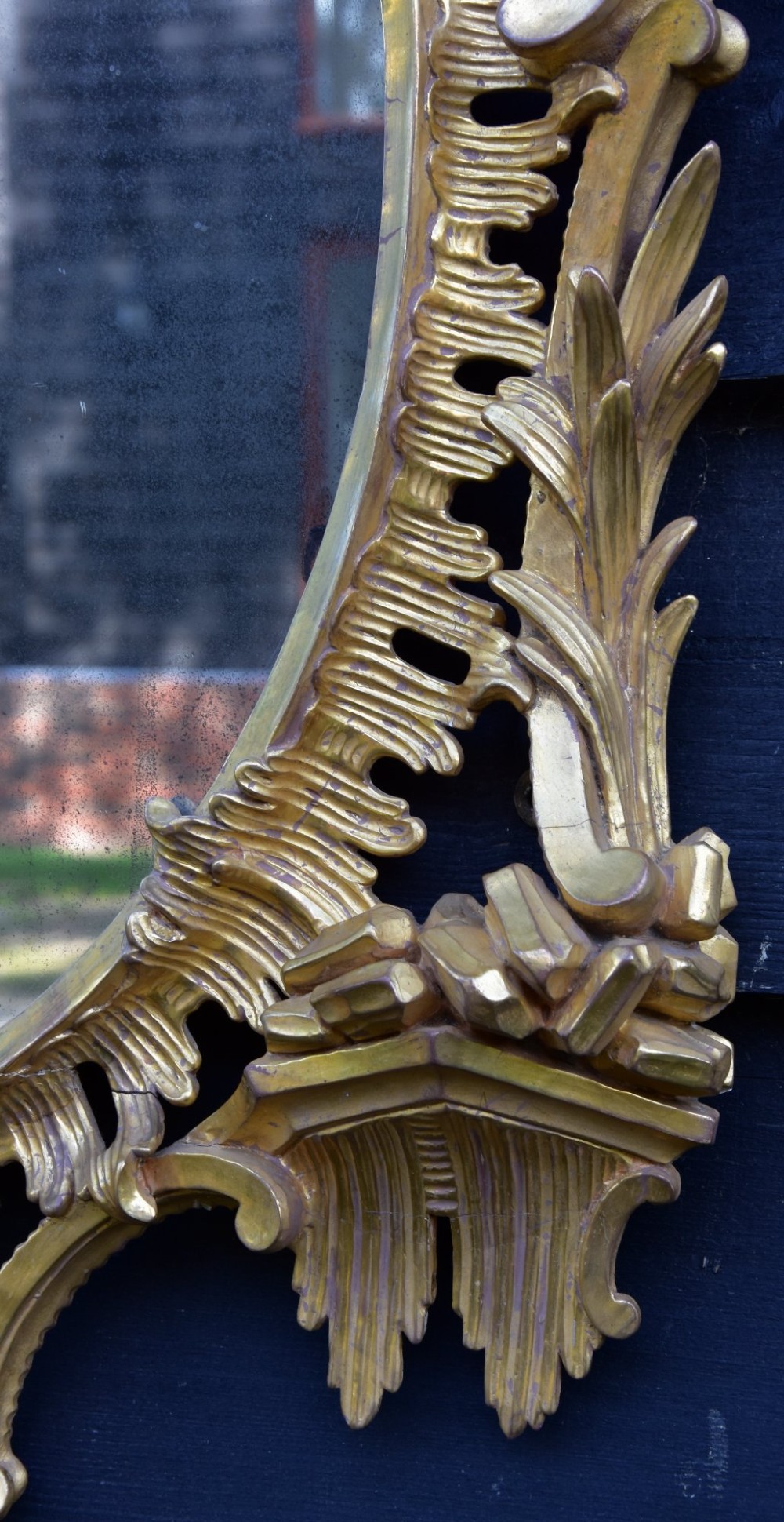 An 18th-century Georgian giltwood wall mirror featuring an oval mirror plate surrounded by an intricately carved gold leaf frame with acanthus leaf cresting and C-scroll motifs. View VI