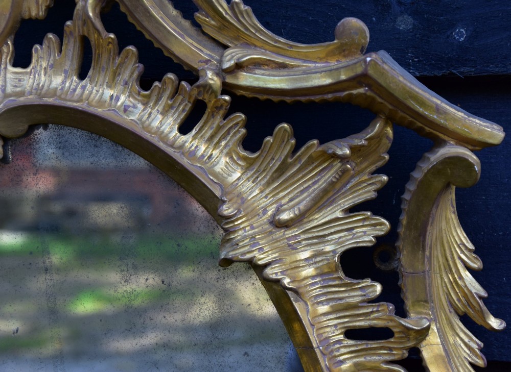 An 18th-century Georgian giltwood wall mirror featuring an oval mirror plate surrounded by an intricately carved gold leaf frame with acanthus leaf cresting and C-scroll motifs. View VIII