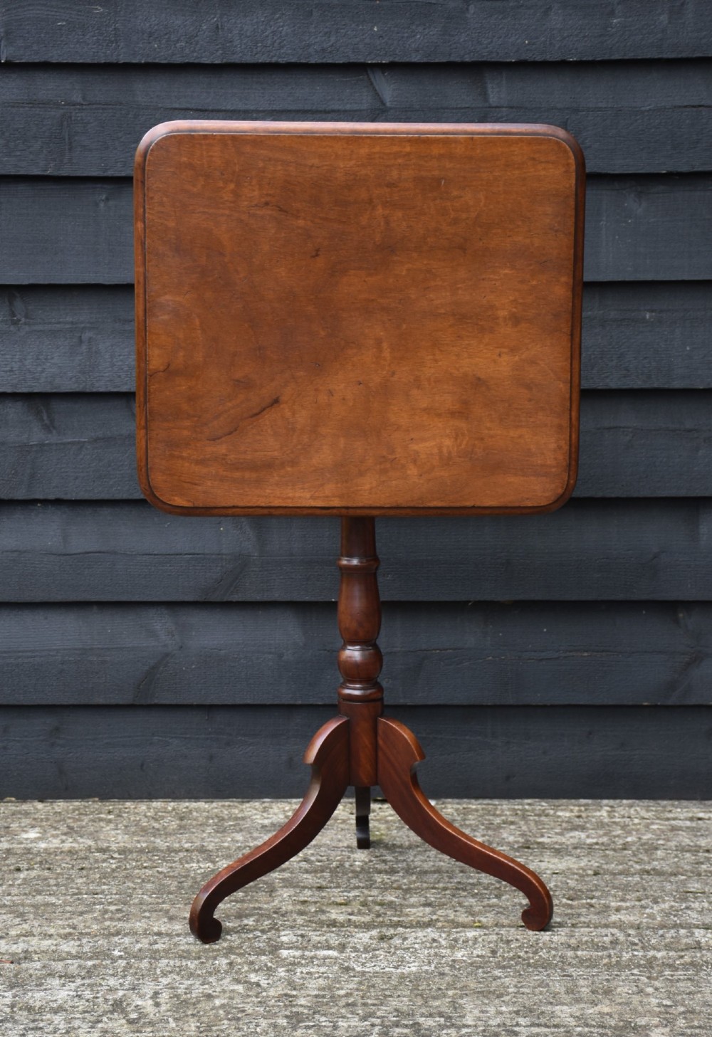 A 19th-century mahogany tilt-top wine table with a rectangular rounded surface, turned pedestal column, and three splayed legs. View II