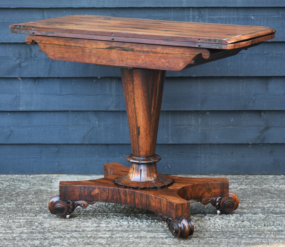 A 19th-century rosewood tea table featuring a rectangular fold-over top, carved scroll brackets, a tapered pedestal column, and a quadform plinth base with scroll feet. View II