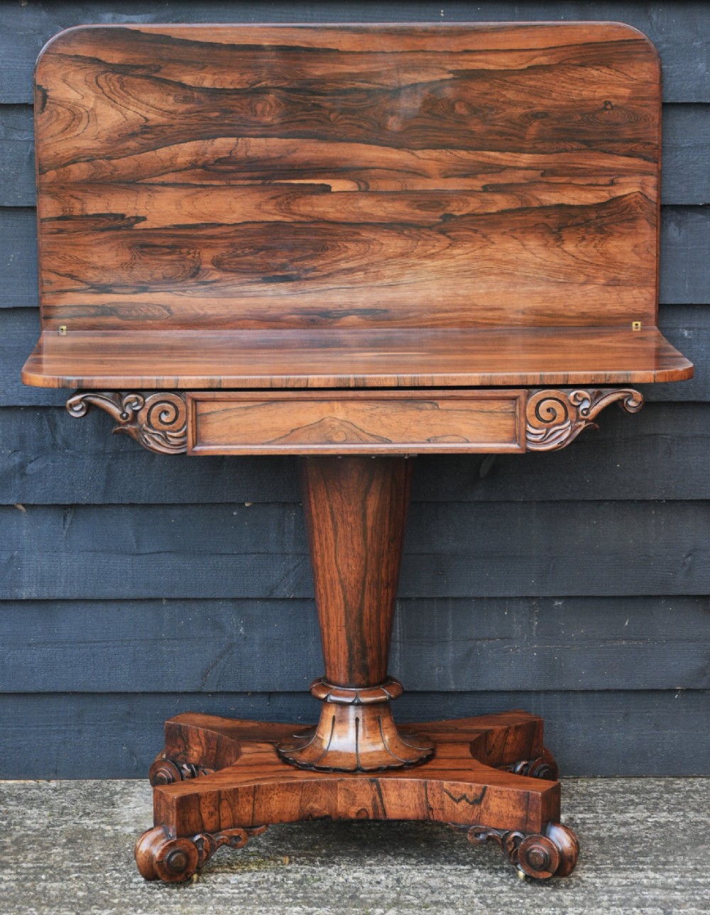 A 19th-century rosewood tea table featuring a rectangular fold-over top, carved scroll brackets, a tapered pedestal column, and a quadform plinth base with scroll feet. View III