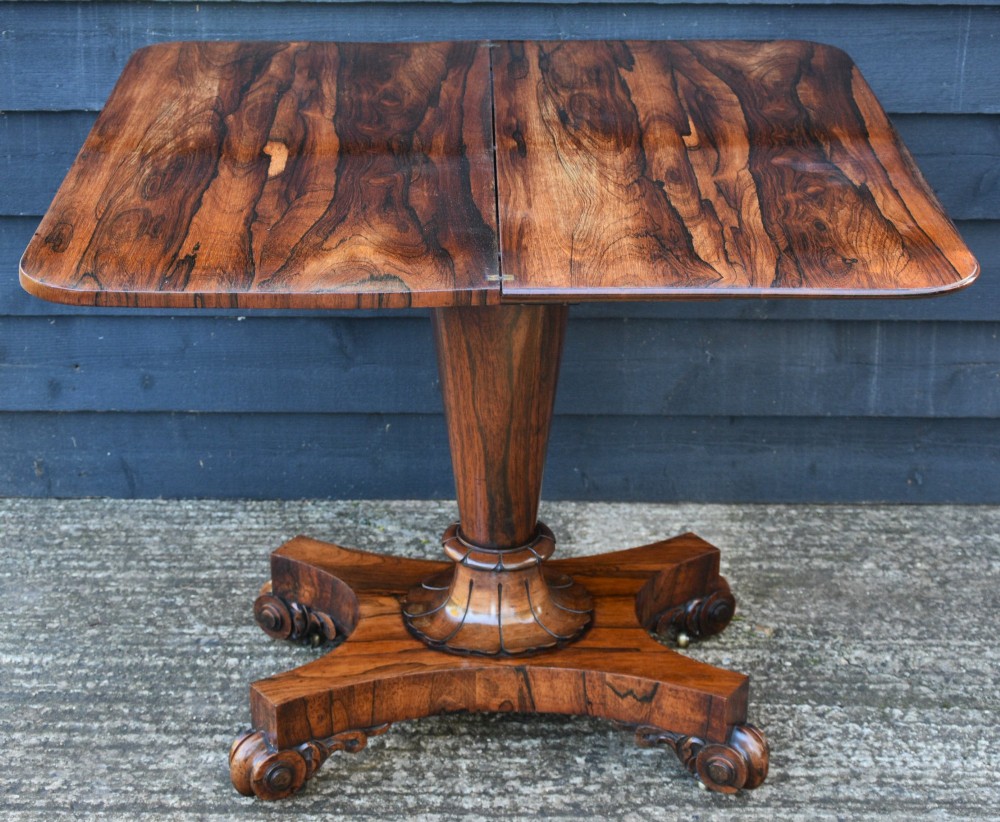 A 19th-century rosewood tea table featuring a rectangular fold-over top, carved scroll brackets, a tapered pedestal column, and a quadform plinth base with scroll feet. View IV