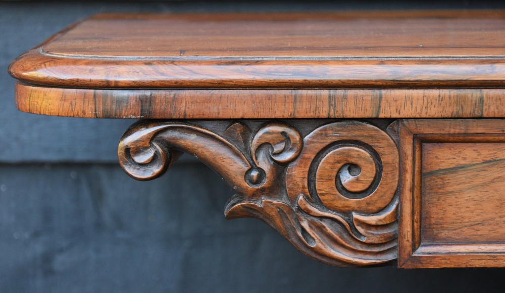 A 19th-century rosewood tea table featuring a rectangular fold-over top, carved scroll brackets, a tapered pedestal column, and a quadform plinth base with scroll feet. View V