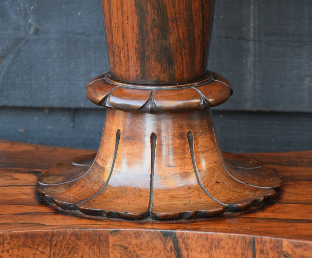 A 19th-century rosewood tea table featuring a rectangular fold-over top, carved scroll brackets, a tapered pedestal column, and a quadform plinth base with scroll feet. View VI