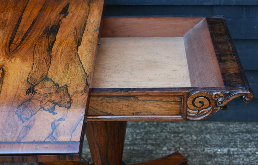 A 19th-century rosewood tea table featuring a rectangular fold-over top, carved scroll brackets, a tapered pedestal column, and a quadform plinth base with scroll feet. View IX