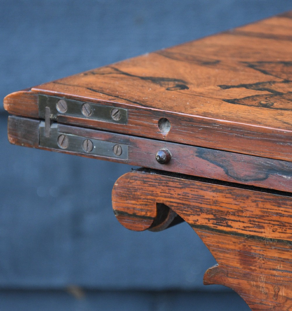 A 19th-century rosewood tea table featuring a rectangular fold-over top, carved scroll brackets, a tapered pedestal column, and a quadform plinth base with scroll feet. View X