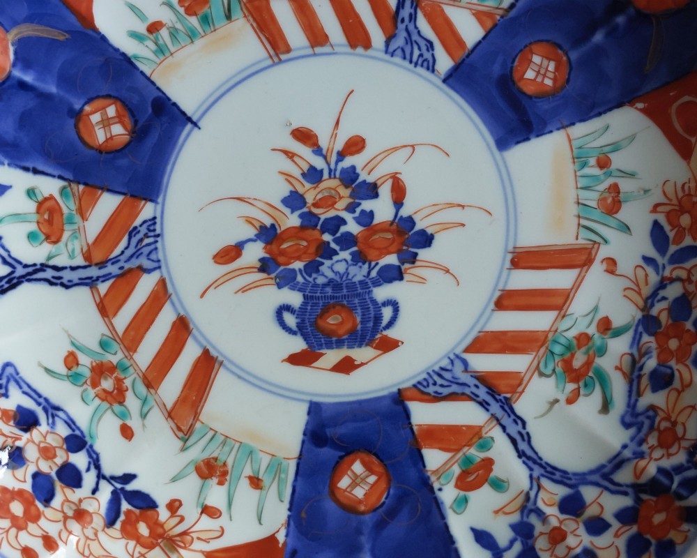 A circular Japanese Imari porcelain plate featuring a scalloped rim, hand-painted cobalt blue and iron-red floral motifs, and broad panels arranged around a central vase design. View II