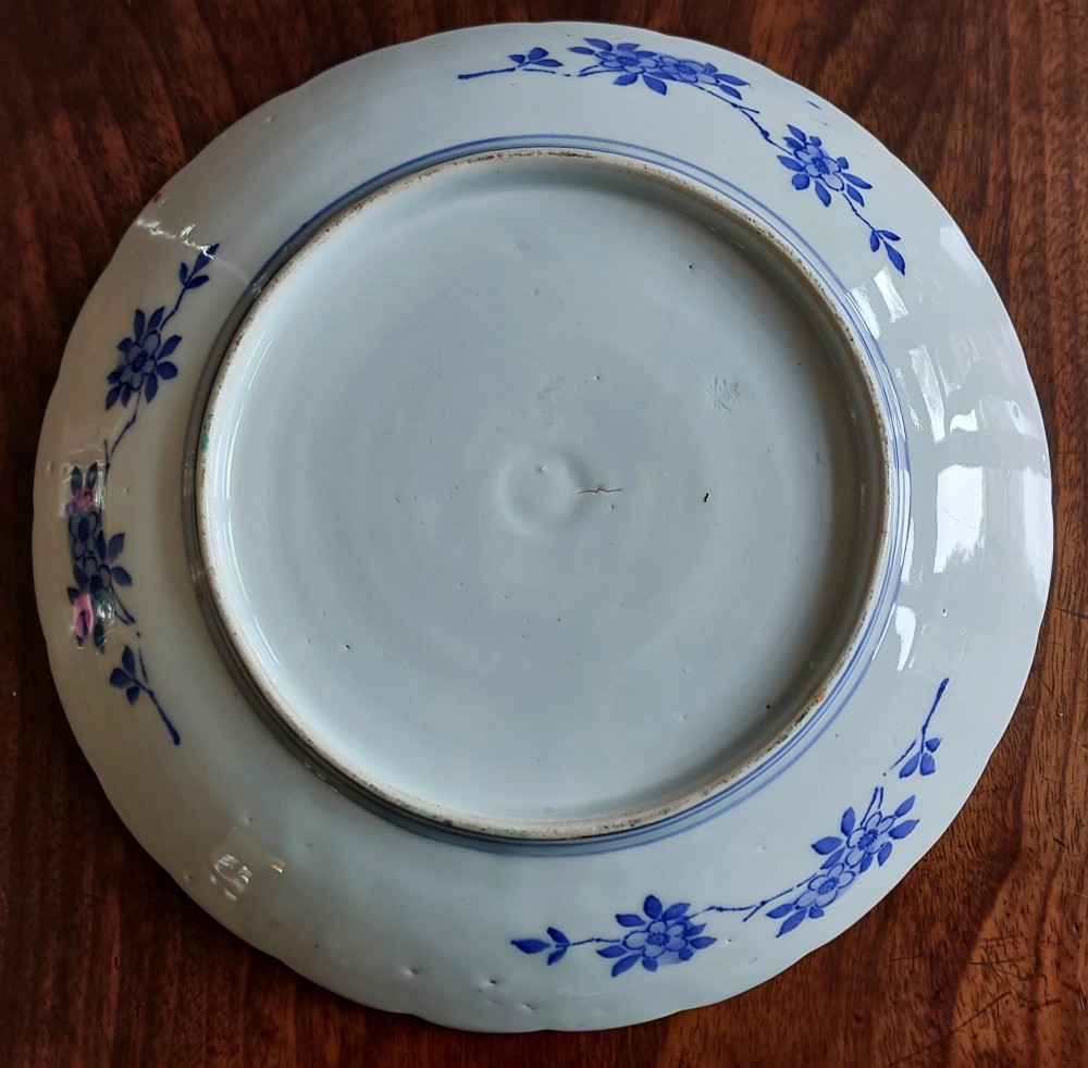 A circular Japanese Imari porcelain plate featuring a scalloped rim, hand-painted cobalt blue and iron-red floral motifs, and broad panels arranged around a central vase design. View IV