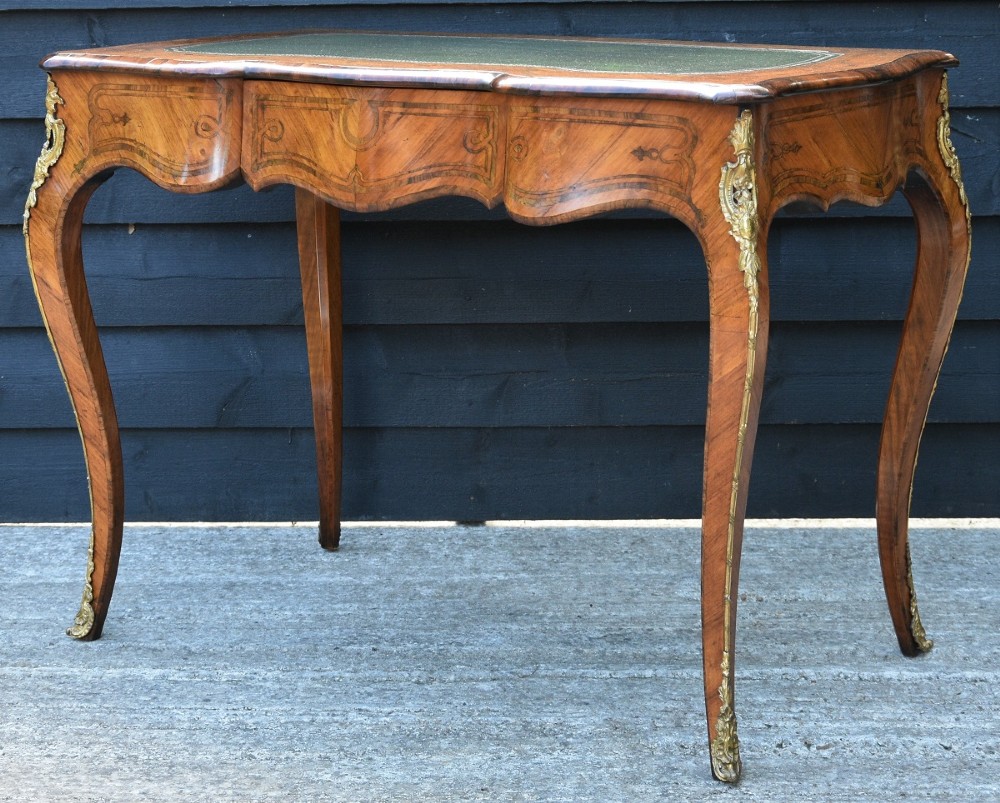 A nineteenth-century French kingwood writing desk featuring a serpentine top, marquetry inlay, slender cabriole legs, and ornate gilt bronze mounts. View V