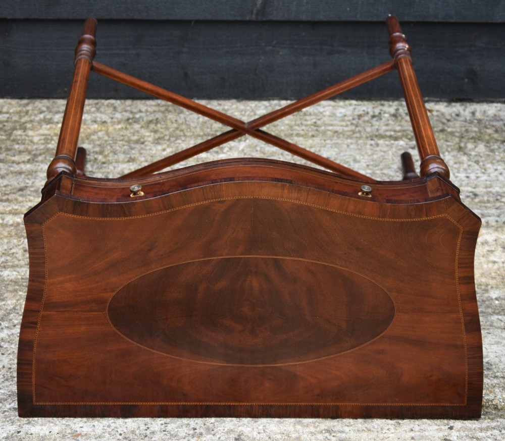 An Edwardian mahogany sewing table featuring a serpentine front with line inlay, slender turned legs connected by an X-frame stretcher, and a pleated cloth basket suspended underneath. View VII