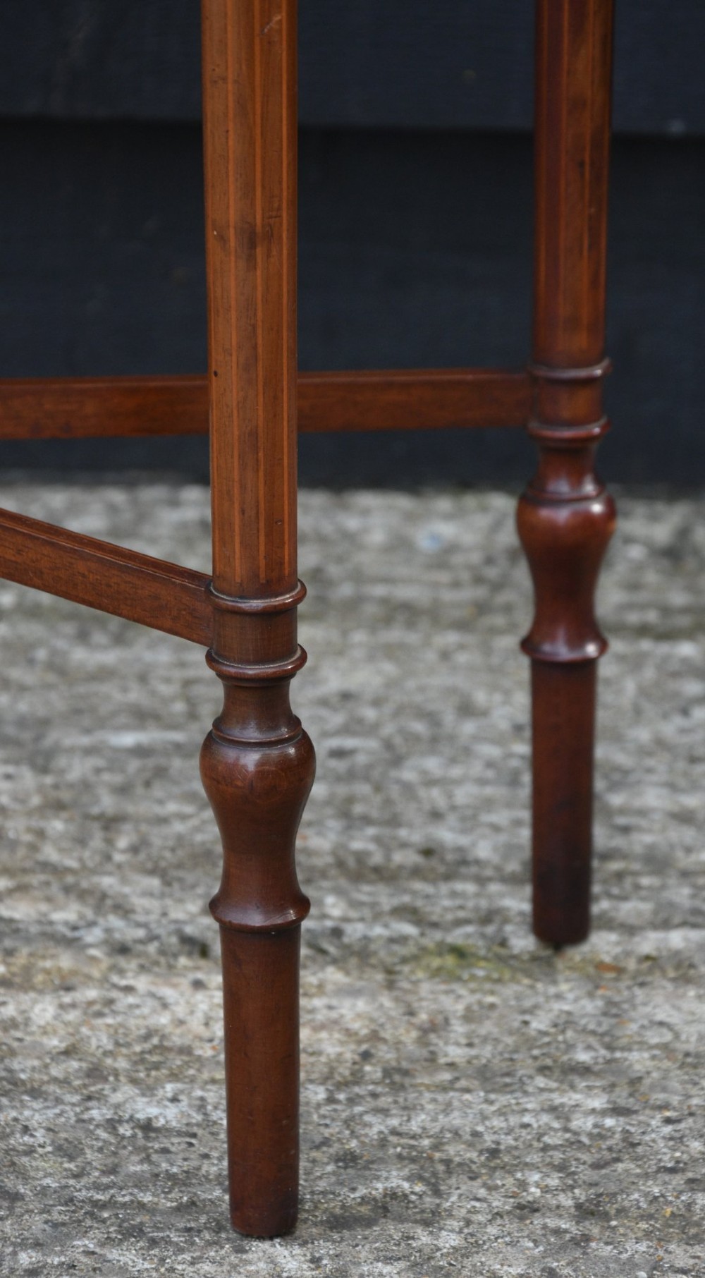 An Edwardian mahogany sewing table featuring a serpentine front with line inlay, slender turned legs connected by an X-frame stretcher, and a pleated cloth basket suspended underneath. View VIII