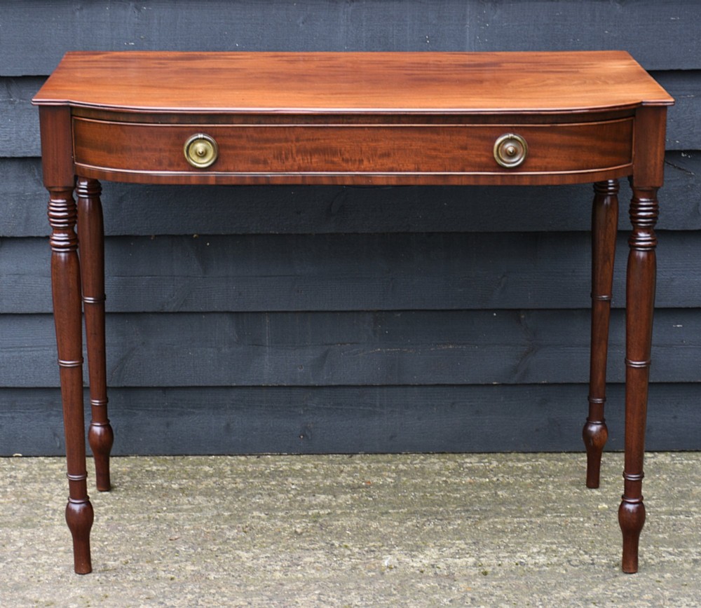 A Regency mahogany bow-fronted side table featuring a single drawer with brass ring handles and four turned tapered legs. View II