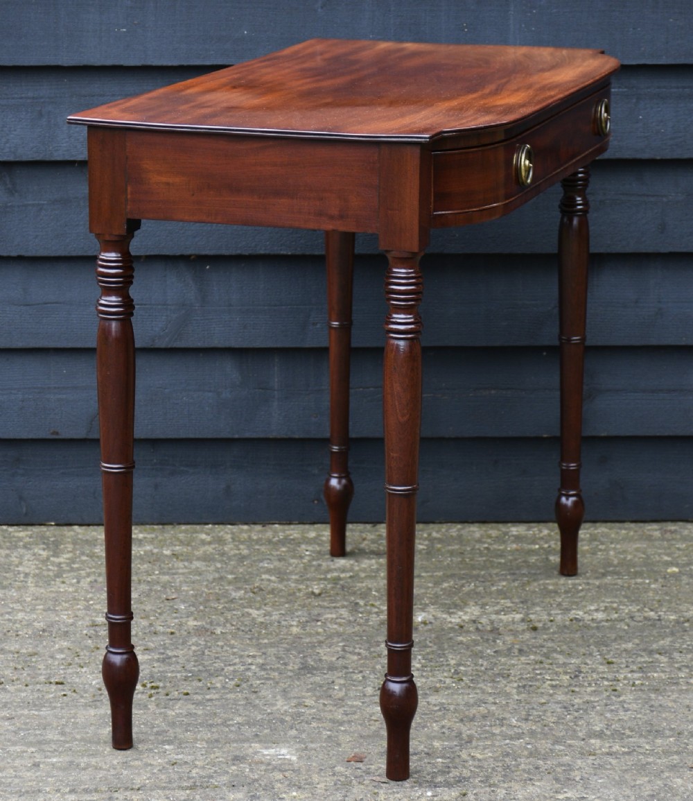 A Regency mahogany bow-fronted side table featuring a single drawer with brass ring handles and four turned tapered legs. View IV