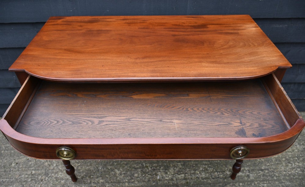 A Regency mahogany bow-fronted side table featuring a single drawer with brass ring handles and four turned tapered legs. View V
