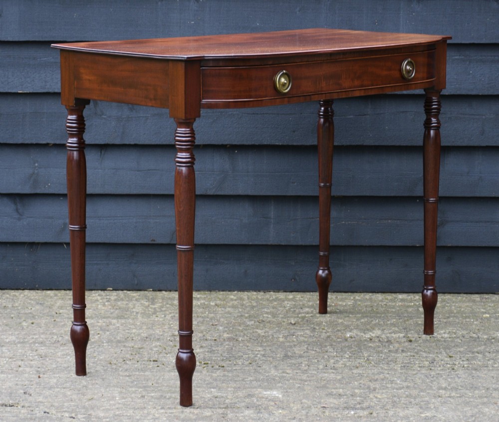 A Regency mahogany bow-fronted side table featuring a single drawer with brass ring handles and four turned tapered legs. View IX