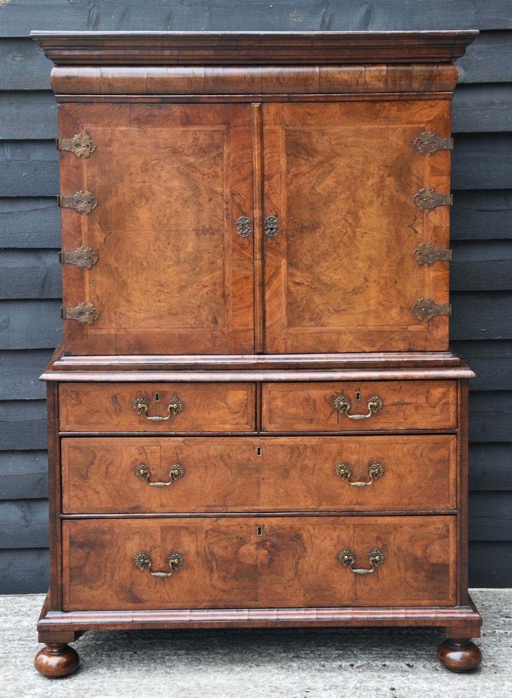A seventeenth-century William and Mary walnut cabinet on chest featuring double doors with decorative brass hinges above three drawers on bun feet.