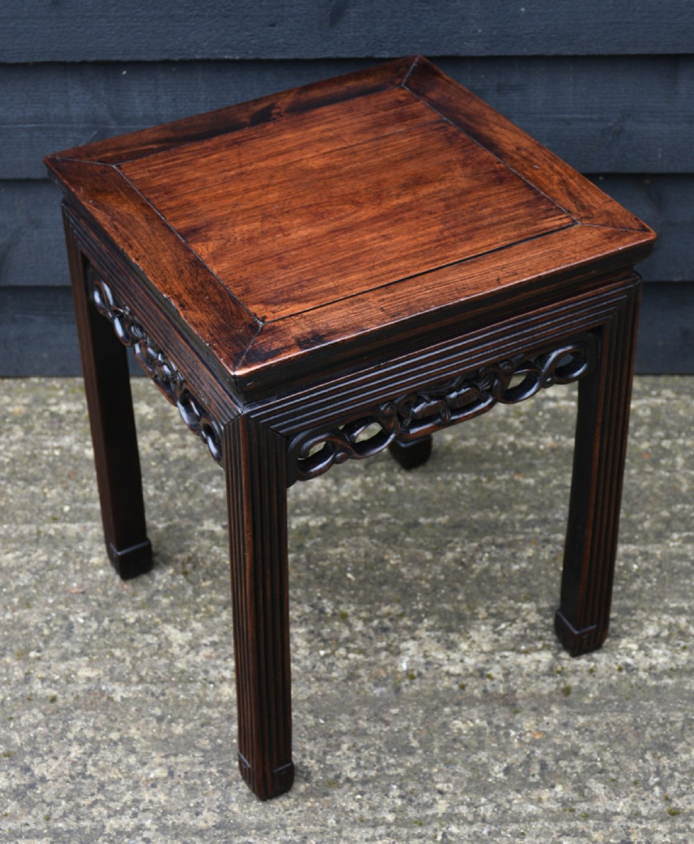A square dark rosewood side table featuring a floating panel top, openwork carved frieze, and reeded legs. View II