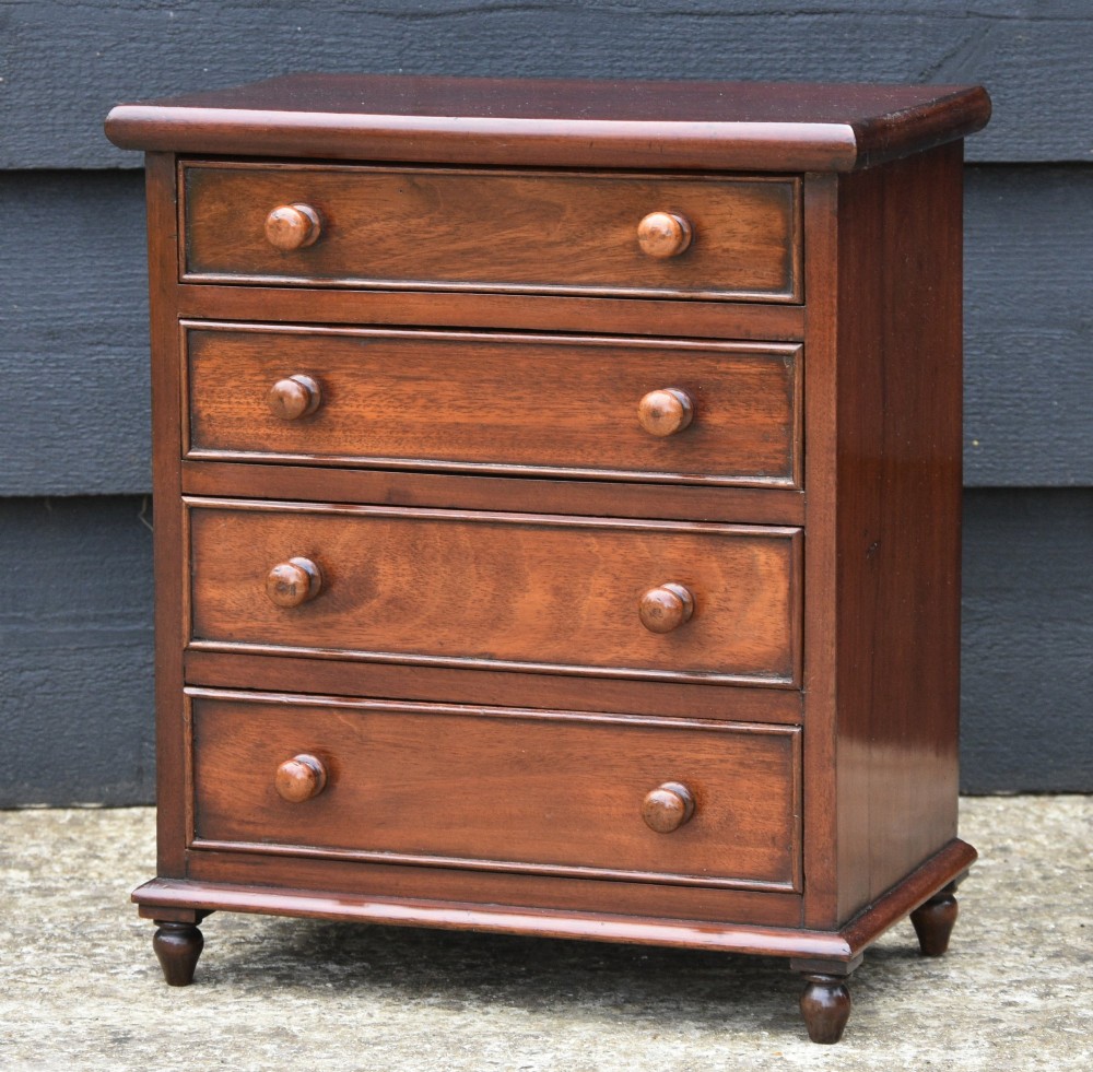A Victorian mahogany miniature chest of drawers featuring four drawers with turned wooden knobs set upon short turned feet.