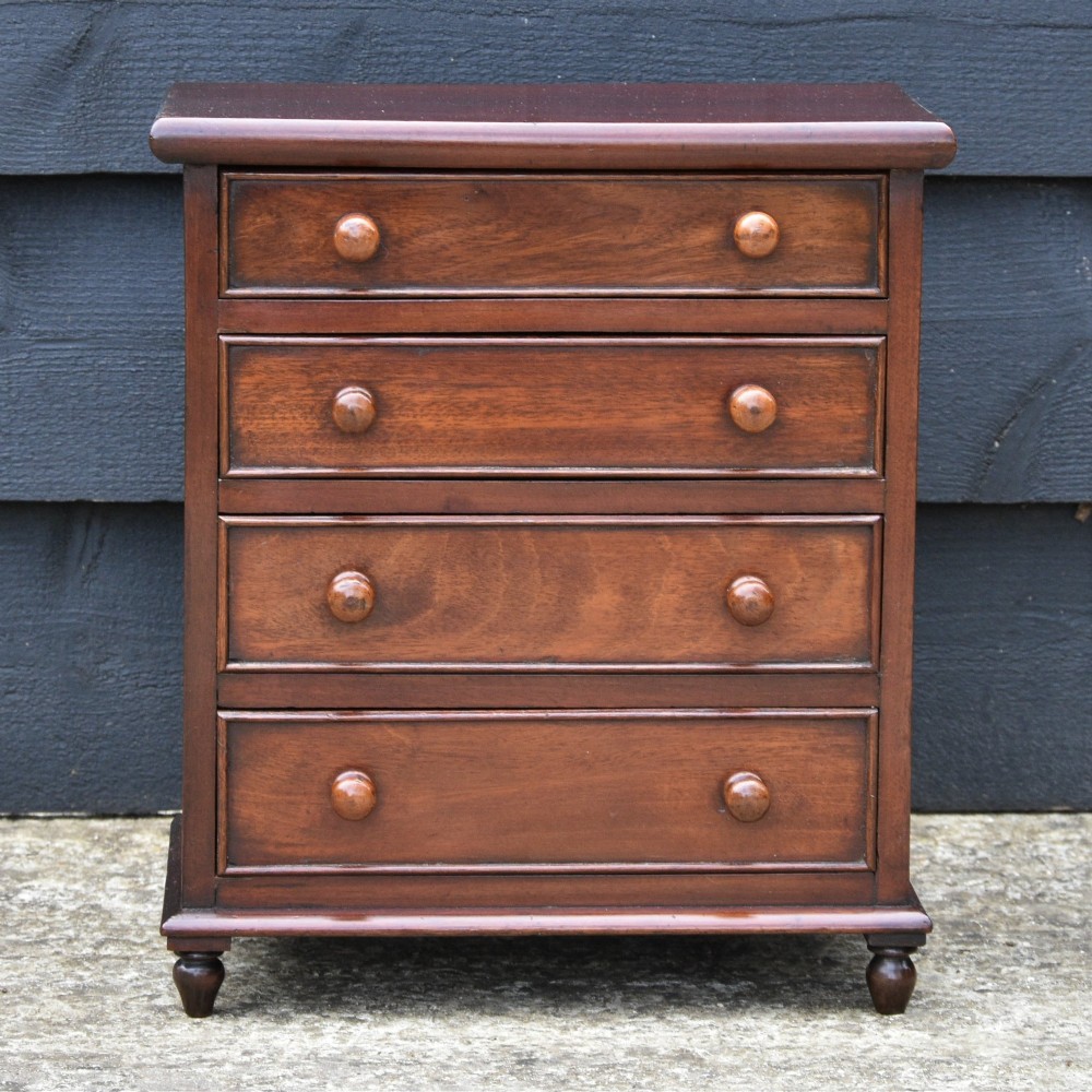 A Victorian mahogany miniature chest of drawers featuring four drawers with turned wooden knobs set upon short turned feet. View II