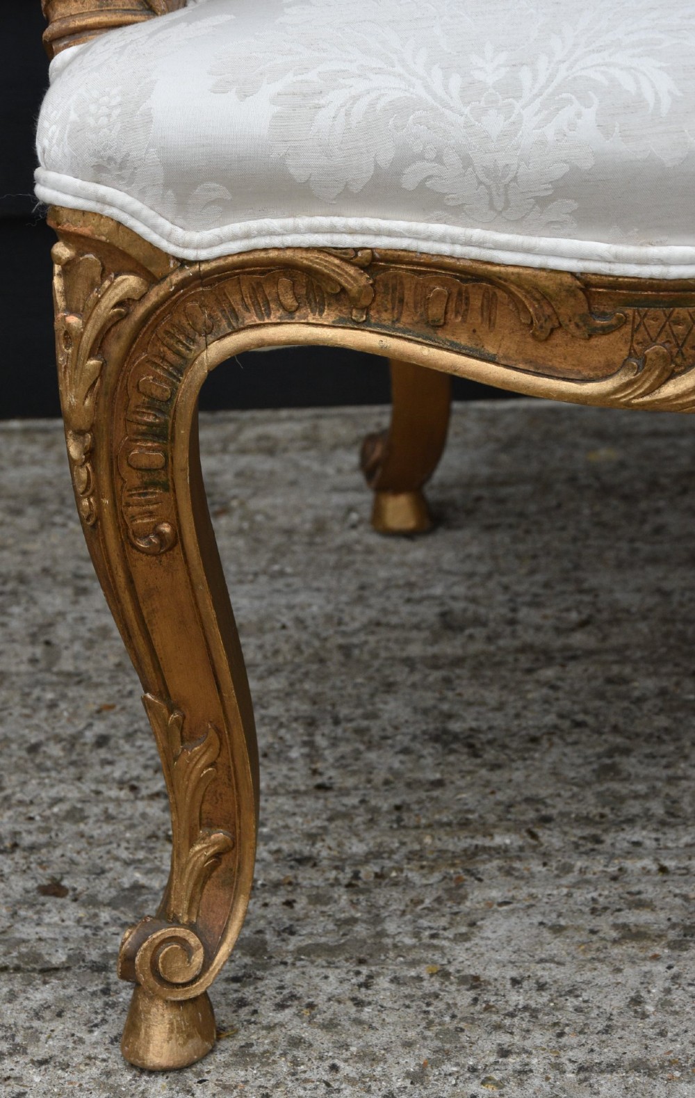 A pair of late 19th-century French giltwood armchairs featuring carved scrolled crestings and upholstered in cream patterned damask fabric. View V