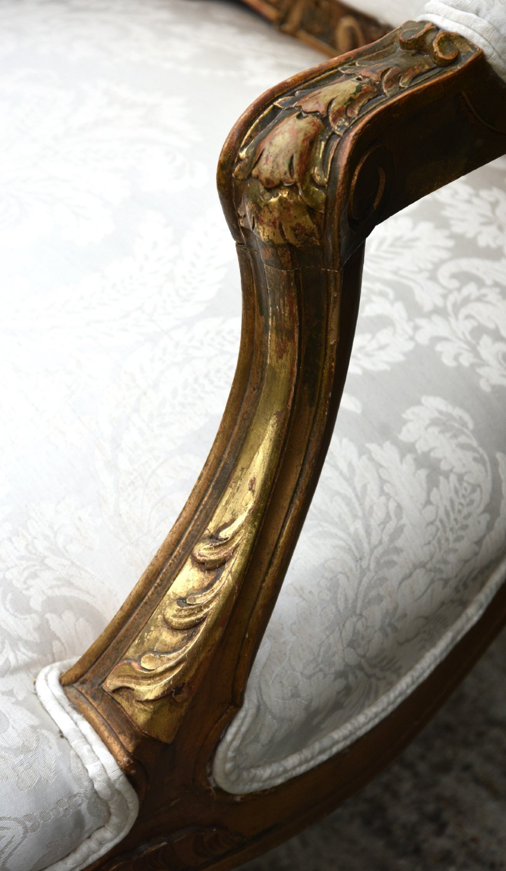 A pair of late 19th-century French giltwood armchairs featuring carved scrolled crestings and upholstered in cream patterned damask fabric. View VII