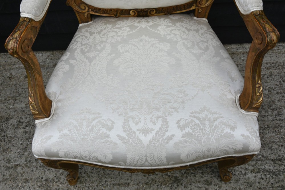 A pair of late 19th-century French giltwood armchairs featuring carved scrolled crestings and upholstered in cream patterned damask fabric. View VIII
