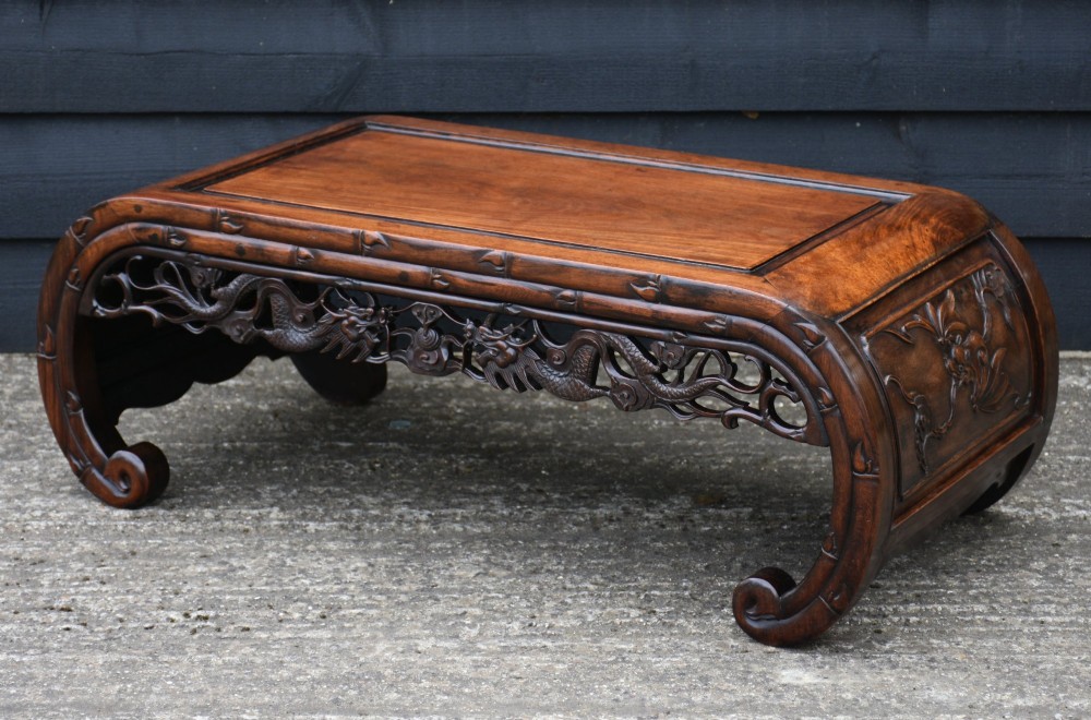 An antique Chinese rosewood low coffee table featuring elaborate openwork dragon carvings on the apron and curved scroll legs with bamboo motif borders.